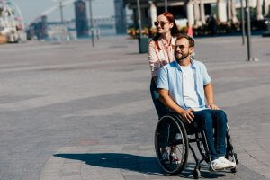 attractive girlfriend in sunglasses pushing disabled handsome boyfriend in wheelchair